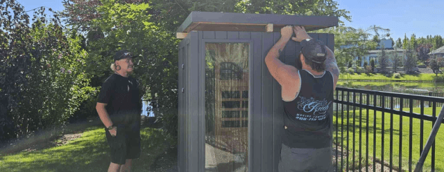 Movers guiding the sauna across a yard